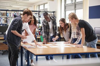 Eine Gruppe von Studierenden steht um einen Tisch und diskutiert